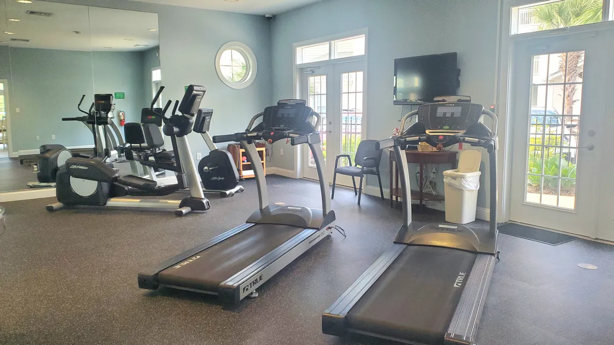 A bright, modern fitness center featuring treadmills, an elliptical machine, large windows for natural light, and a mirrored wall. The space looks energetic and spacious, encouraging an active lifestyle for guests.