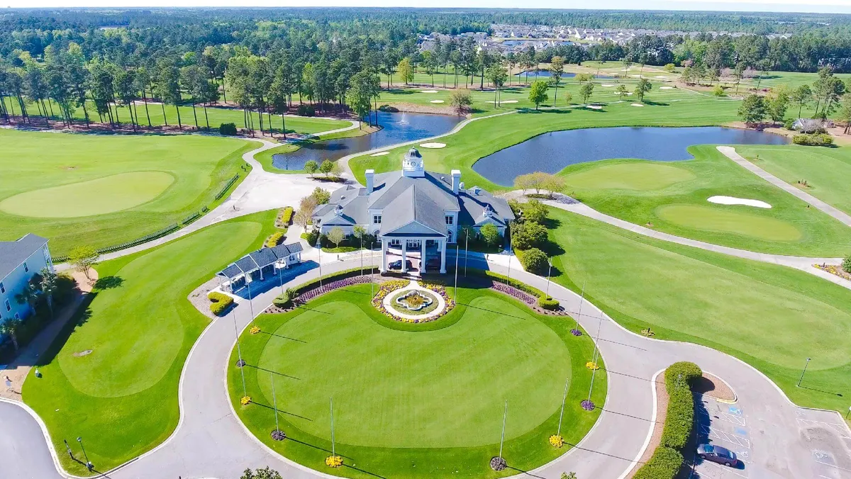 An inviting exterior shot highlighting the grand clubhouse, lush landscaped gardens, glimpses of the adjacent golf course, and shimmering water features. The tranquil setting captures the serene atmosphere and the vibrant social life surrounding the course, ideal for both play and relaxation.