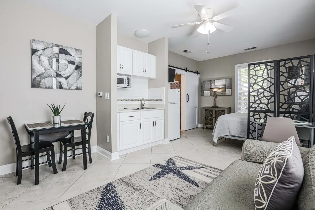 A wide-angle view of the living area displays the compact kitchenette, a small dining table, a comfortable sofa, and a decorative screen. The space is arranged for both relaxation and shared meals, with functional furnishings and cozy decorative touches.