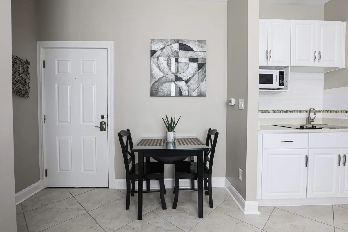 A sleek black dining table is the focal point, framed by geometric wall art and surrounded by crisp, white cabinetry. The space is inviting and contemporary, ideal for casual breakfasts or meaningful conversations over coffee.