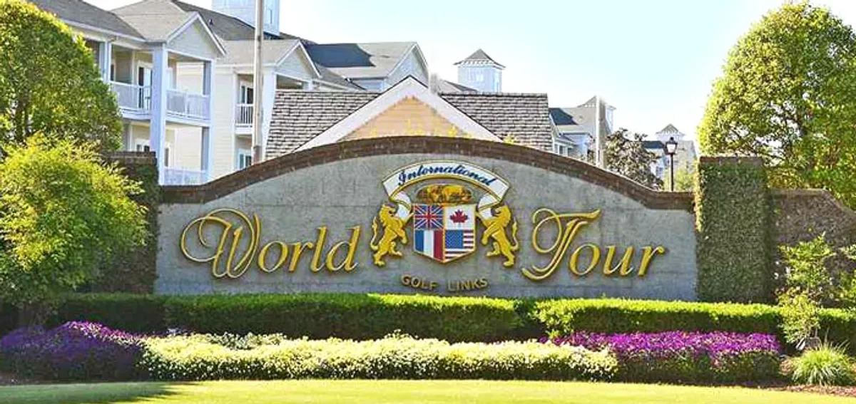 A welcoming exterior view of the entrance sign to the World Tour Golf Course, surrounded by manicured landscaping and the opening stretch of the greens. The scene conveys a sense of arrival and sets the tone for an elegant and relaxed golfing experience.
