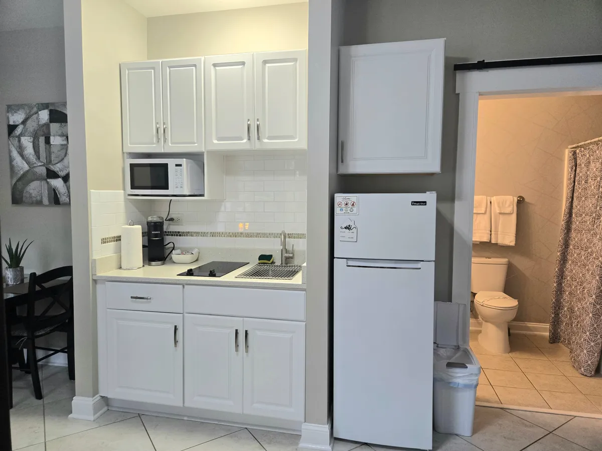 The kitchenette is the focal point in this inviting, functional space, complete with modern appliances like a microwave and refrigerator. The arrangement is practical for preparing meals or snacks, with a view toward the bathroom entrance, reinforcing convenience.