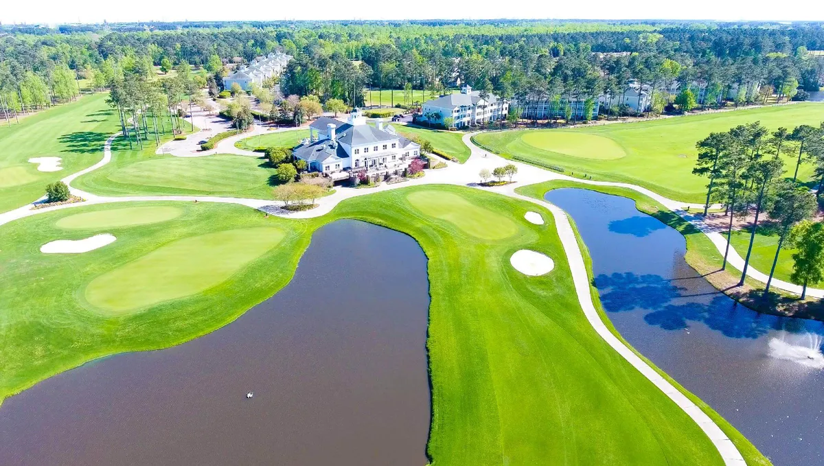 A panoramic exterior shot featuring the elegant clubhouse overlooking a manicured golf course, detailed water features, and vibrant greenery. The scene is tranquil and luxurious, highlighting scenic views and the clubhouse’s central role.