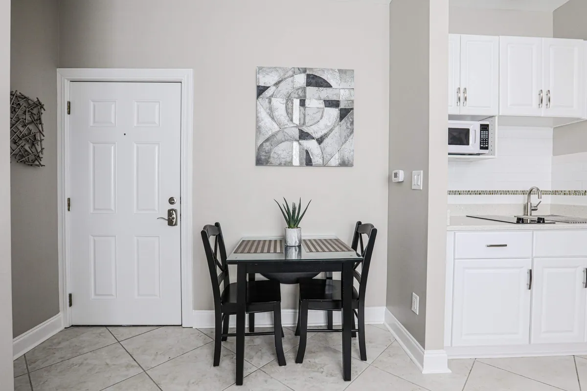 A cozy, modern dining area featuring a small dining table set for two, complemented by abstract wall art and a view into the kitchen area. The scene suggests a space for casual dining or morning coffee, with stylish decor that encourages conversation and relaxation.